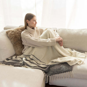 Frau kuschelt auf Sofa mit Alpaka Boucle Wolldecke MULLIDA