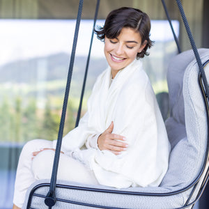 Frau kuschelt im Hängestuhl mit Plaid SEDA aus Alpakawolle im Beigeton