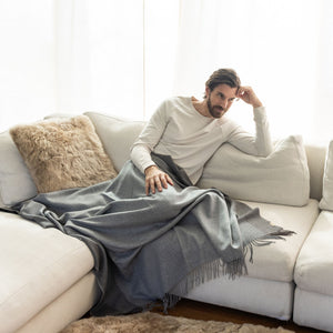 Mann sitzt auf dem Sofa mit Plaid TIRA in dunkelgrau