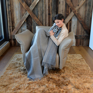 Frau sitzt auf einem Sessel mit Plaid TIRA in dunkelgrau