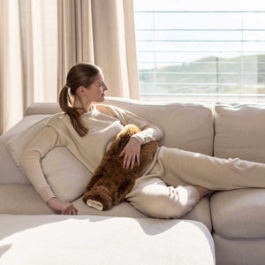 Woman relaxing with tubular alpaca hot water bottle near window 