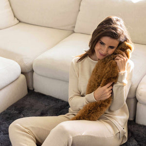 Frau sitzt angelehnt am Sofa und kuschelt mit Schlauchwärmflasche TUBO